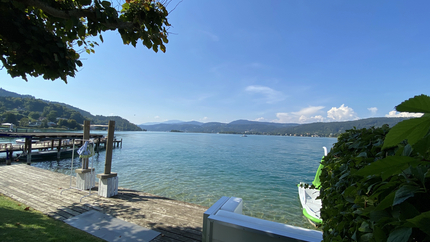 See mit Steg, grünem Ufer und Bergen bei klarem Himmel