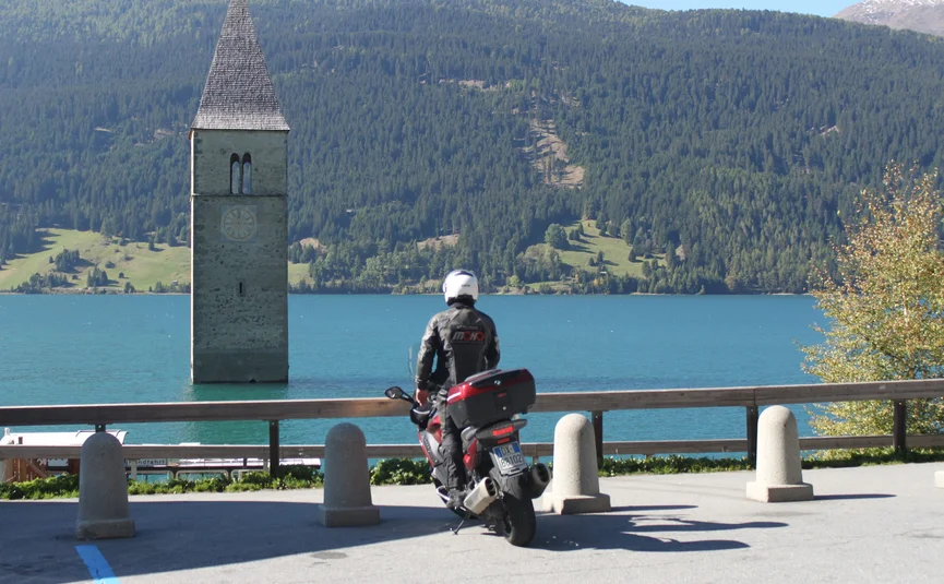 Motorcyclist looking at tower in lake with forested mountains