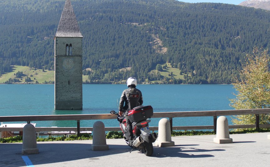 Hotel am Reschensee *** © The Dilitz Company GmbH Motorradfahrer blickt auf Turm im See vor bewaldeten Bergen