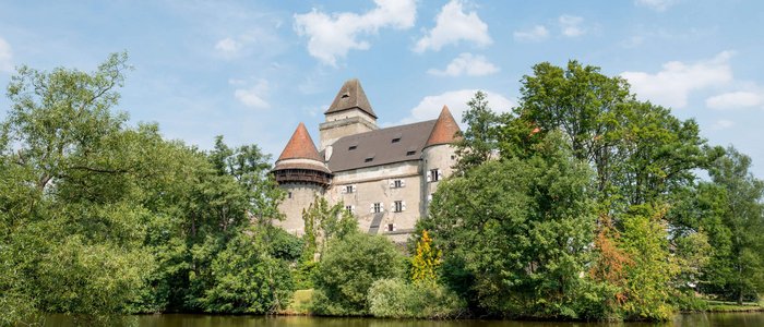 Mittelalterliches Schloss mit Türmen hinter Bäumen an einem See