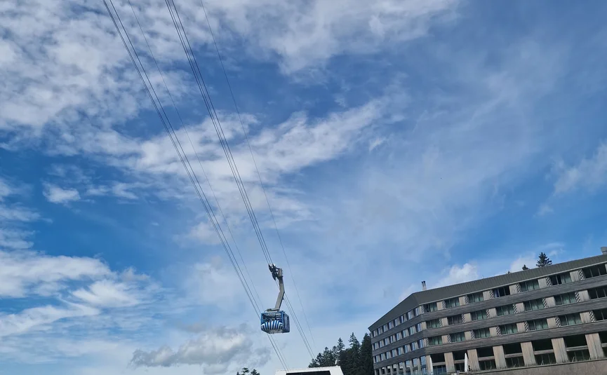 Cable car over green hill with motorcycles and large building in background
