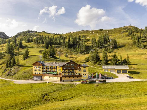 Almhotel & Genussgasthof Hierzegger © Alexander Seger Hotel in grüner Berglandschaft mit Sessellift und Traktor im Vordergrund