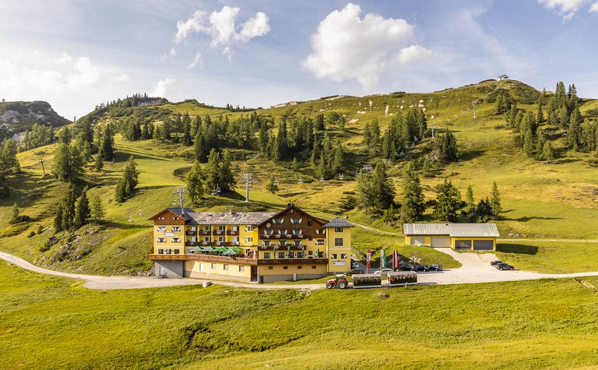 Almhotel & Genussgasthof Hierzegger ***S © Alexander Seger Hotel in grüner Berglandschaft mit Sessellift und Traktor im Vordergrund