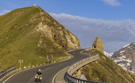 Motorradfahrer auf kurviger Bergstraße mit Aussicht auf schneebedeckte Gipfel
