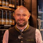 Mann in Tracht hält vier Flaschen Raben Original Likör im Laden