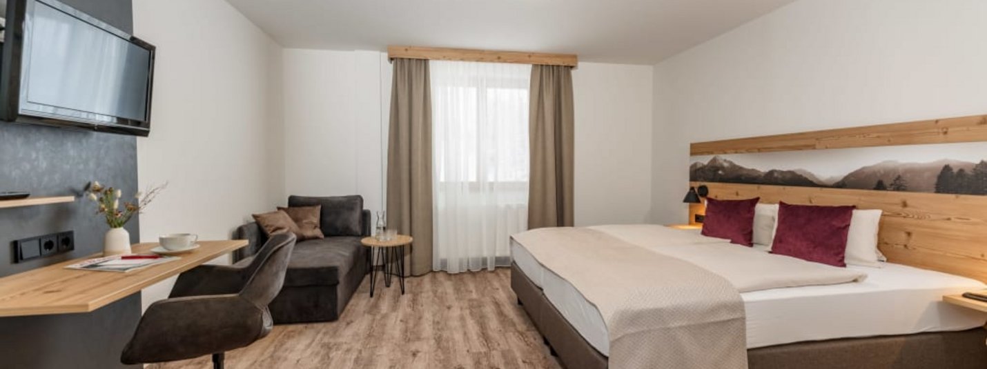 Modern eingerichtetes Hotelzimmer mit Doppelbett, Schreibtisch und Sofa