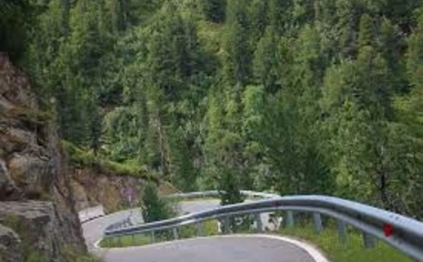 Kurvige Bergstraße mit Leitplanke und Wäldern im Hintergrund