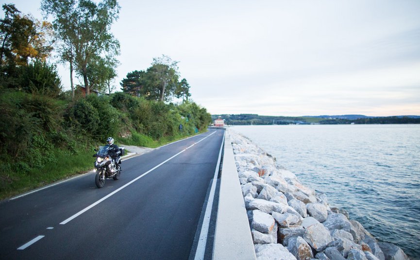 Motorradfahrer auf Küstenstraße neben Felsen und Wasser