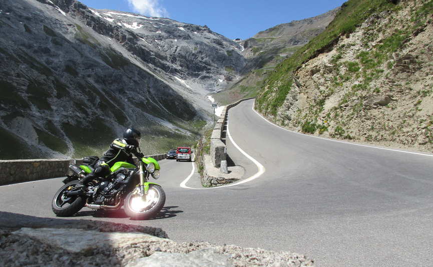 MoHo Schönauer Hof- Tour 12 Stilfserjoch Umbrail Motorcyclist on winding mountain road with steep rocky cliffs and blue sky