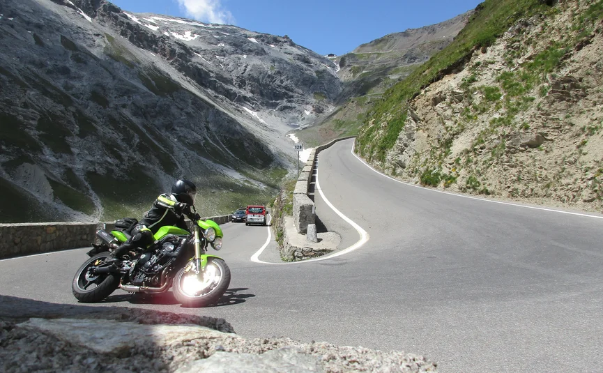 Motorcyclist on winding mountain road with steep rocky cliffs and blue sky