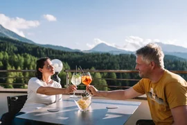 Ein Paar stößt mit Getränken auf Terrasse mit Bergblick an