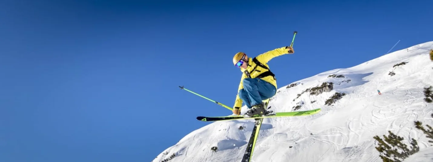 Mid-Week-Skitage 4 Skifahrer in gelber Jacke springt an schneebedecktem Berg unter blauem Himmel