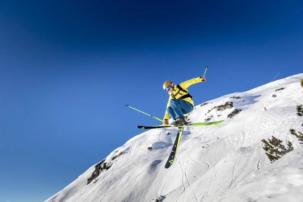 Skier wearing yellow jacket jumps on snowy mountain under clear blue sky