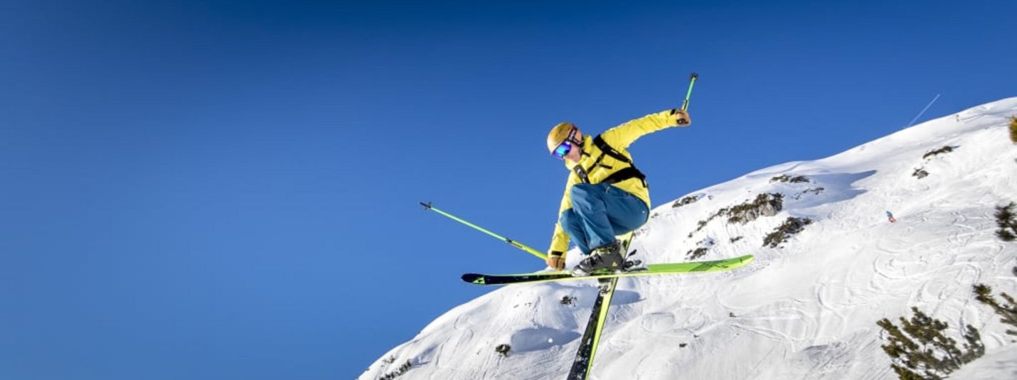 Skifahrer in gelber Jacke springt an schneebedecktem Berg unter blauem Himmel