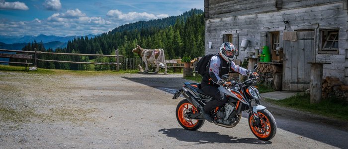 Motorradfahrer vor hölzernem Haus in Berglandschaft unter blauem Himmel