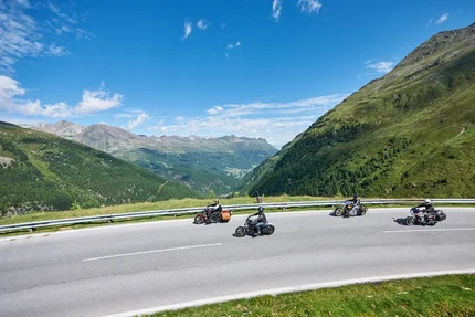 Vier Motorradfahrer fahren auf kurviger Bergstraße bei klarem Himmel
