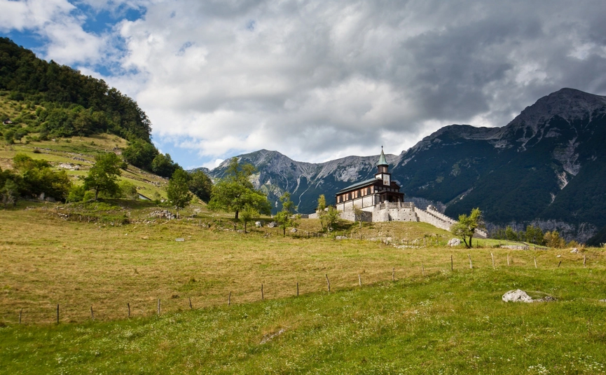 Emerald Soča River & Alpine Peaks Tour Church on a hill with mountains and cloudy sky in the background