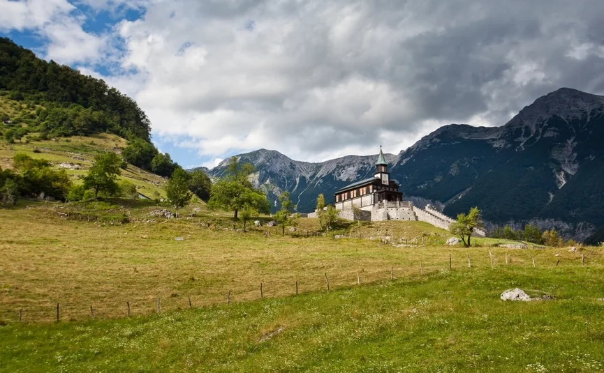 Kirche auf einem Hügel mit Bergen und bewölktem Himmel im Hintergrund
