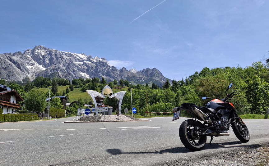 Motorrad an einem Kreisverkehr vor Berglandschaft mit blauem Himmel