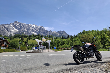 Motorrad an einem Kreisverkehr vor Berglandschaft mit blauem Himmel