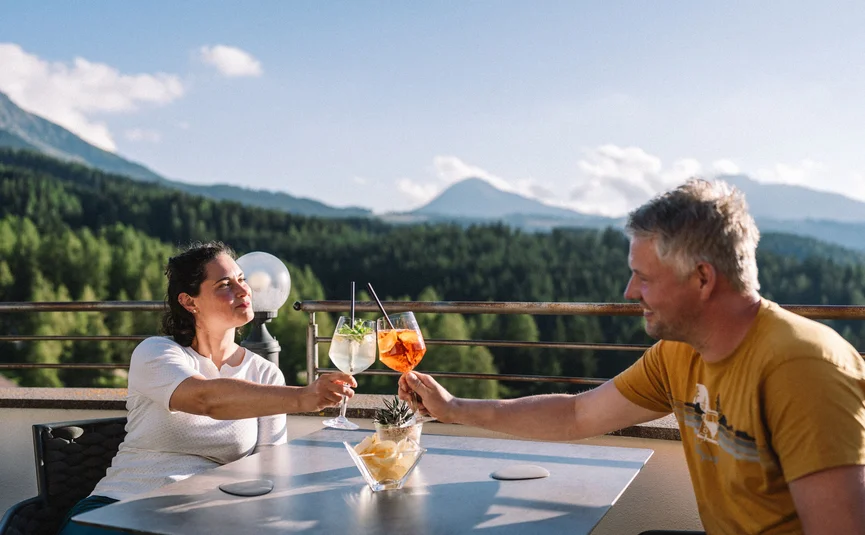 Couple clinking drinks on terrace with mountain scenery