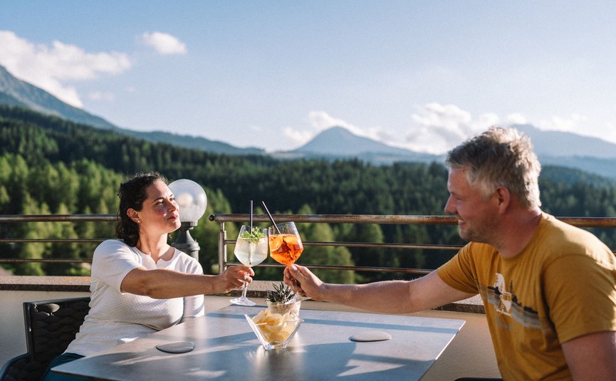 Paar stößt mit Getränken auf Terrasse mit Bergblick an