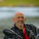 Mühlviertel © Moppetfoto.de Lächelnder Mann in Motorradjacke mit See im Hintergrund