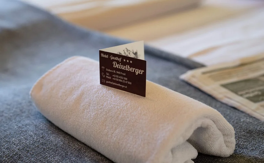 Towel with Deixelberger Hotel business card on a bed