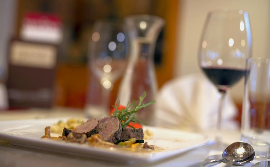 Babymoon im Hotel Rockenschaub Fein angerichtetes Fleischgericht mit Rotwein und Besteck auf einem gedeckten Tisch