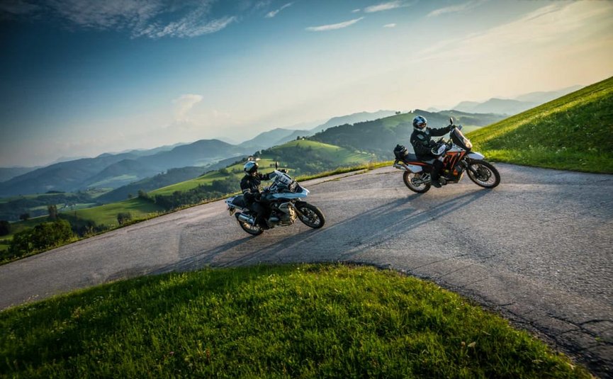 Zwei Motorradfahrer auf kurviger Landstraße in grünen Hügeln bei Sonnenuntergang