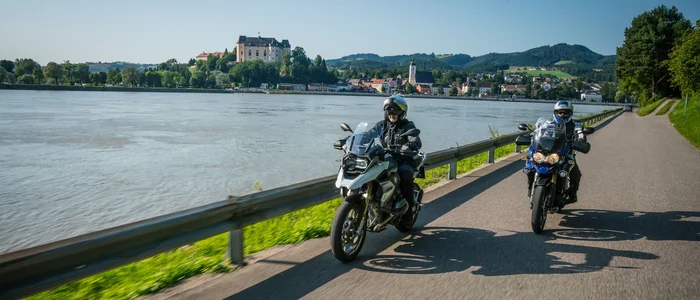 Mühlviertel © Moppetfoto.de Zwei Motorradfahrer fahren neben einem Fluss mit einer Burg im Hintergrund