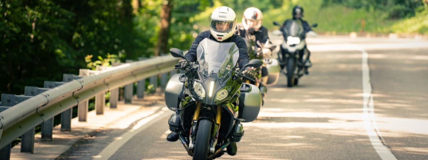 Motorrad - "Land & Leute" Motorradfahrer auf kurviger Straße mit grünem Wald im Hintergrund