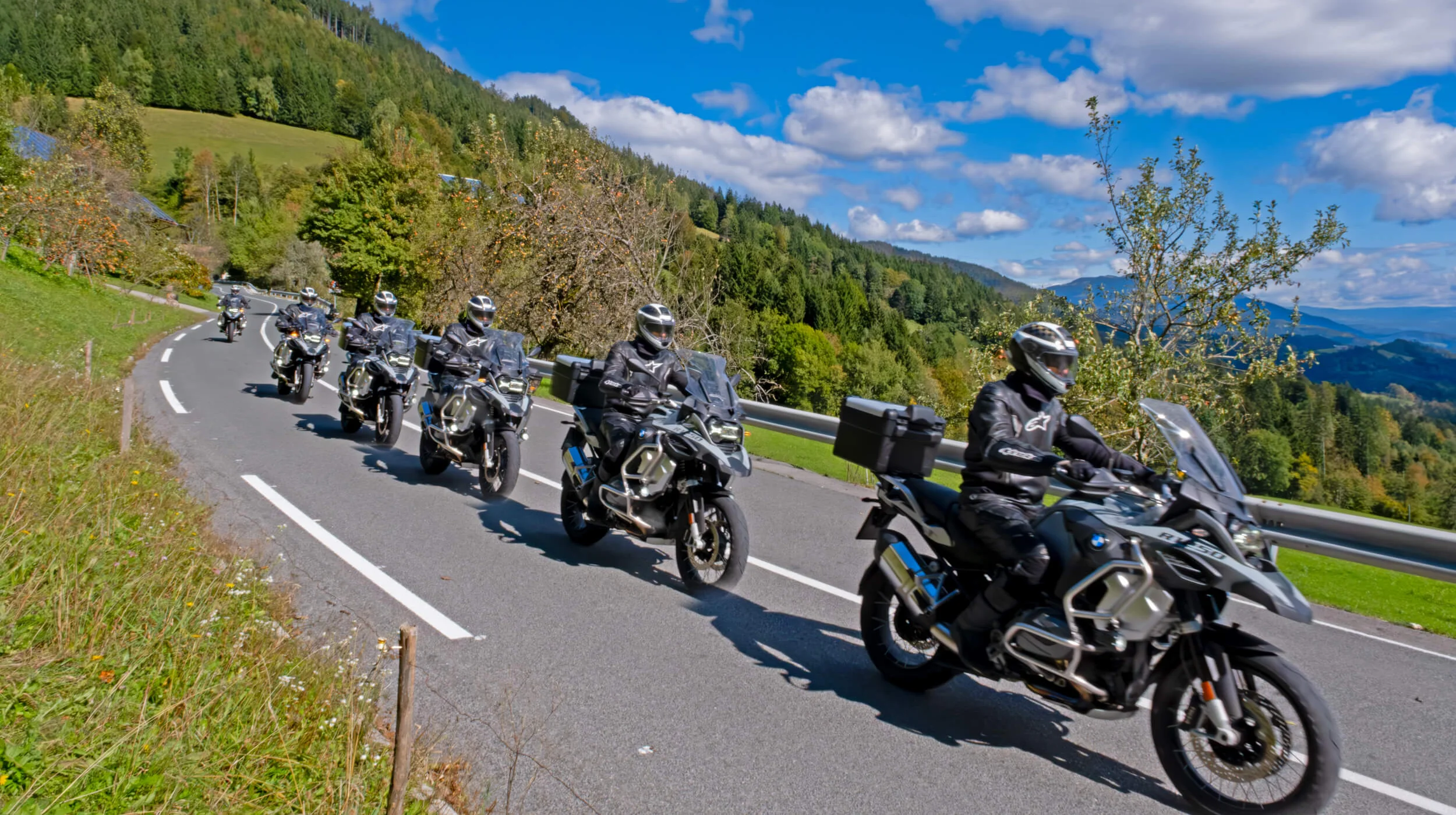 Group of motorcyclists riding on winding rural road in mountainous landscape on sunny day