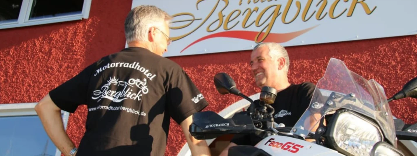 Saisoneröffnung 2022 Zwei Männer neben einem BMW-Motorrad vor dem Schild des Hotels Bergblick