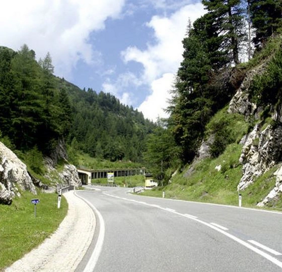 Landstraße durch bewaldete Berge mit Felsen und blauem Himmel