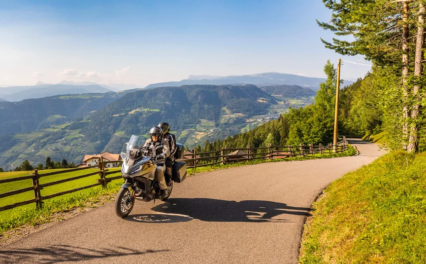 Two motorcyclists riding on mountain road with green valleys and hills