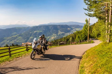 Twee motorrijders op bergweg met uitzicht op groene valleien en heuvels
