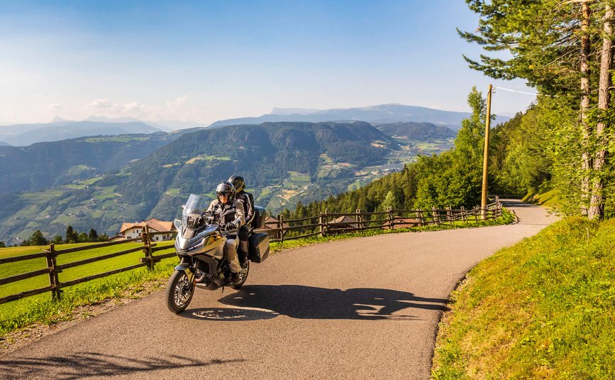 Zwei Motorradfahrer auf Bergstraße mit Blick auf grüne Täler und Berge