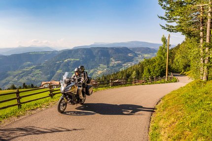 Zwei Motorradfahrer auf Bergstraße mit Blick auf grüne Täler und Berge