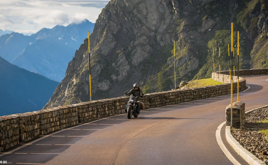 Motorcyclist riding on winding mountain road with stone wall and mountains