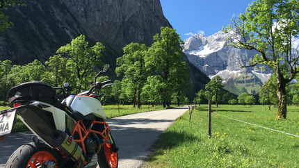 Motorrad auf Straße mit Bergen und grünen Bäumen im Sonnenschein