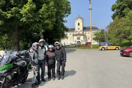 Four motorcyclists posing in front of a castle on a sunny day