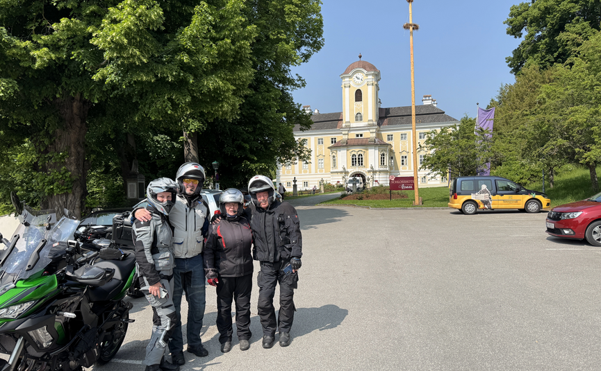Vier Motorradfahrer vor einem Schloss an einem sonnigen Tag