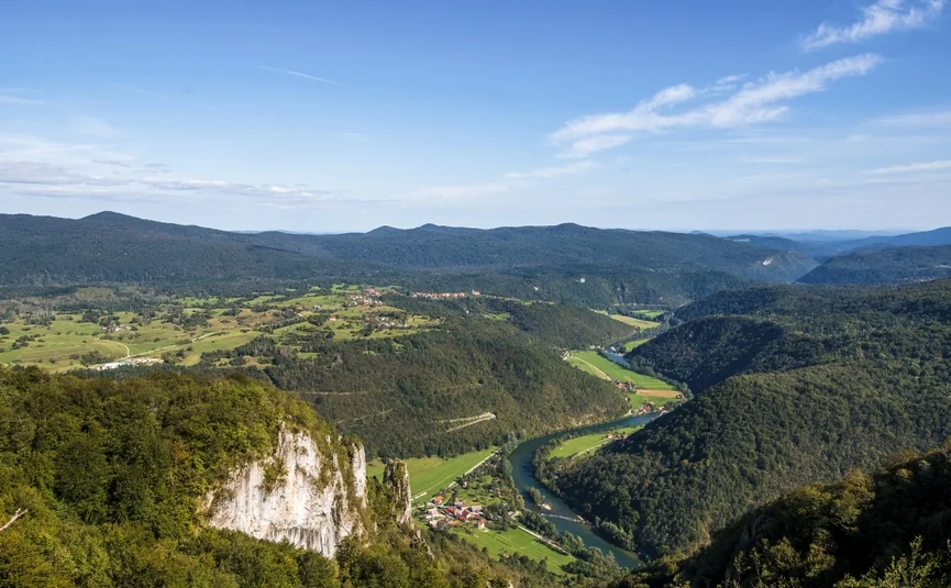 Fluss schlängelt sich durch grünes Tal inmitten bewaldeter Hügel und Berge