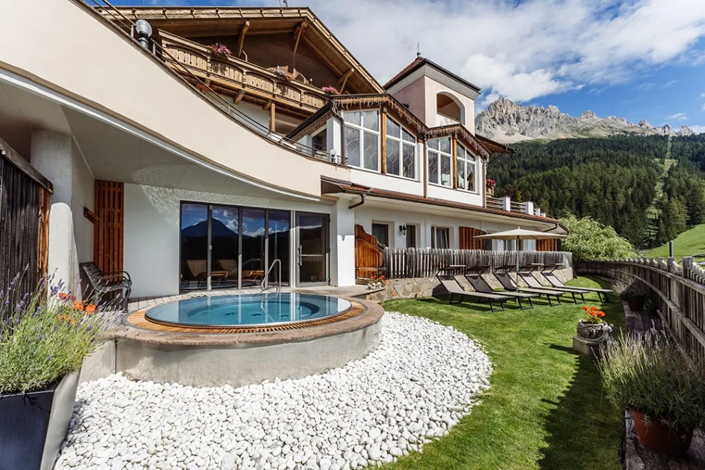 House with hot tub, lounge chairs, and mountain view in summer