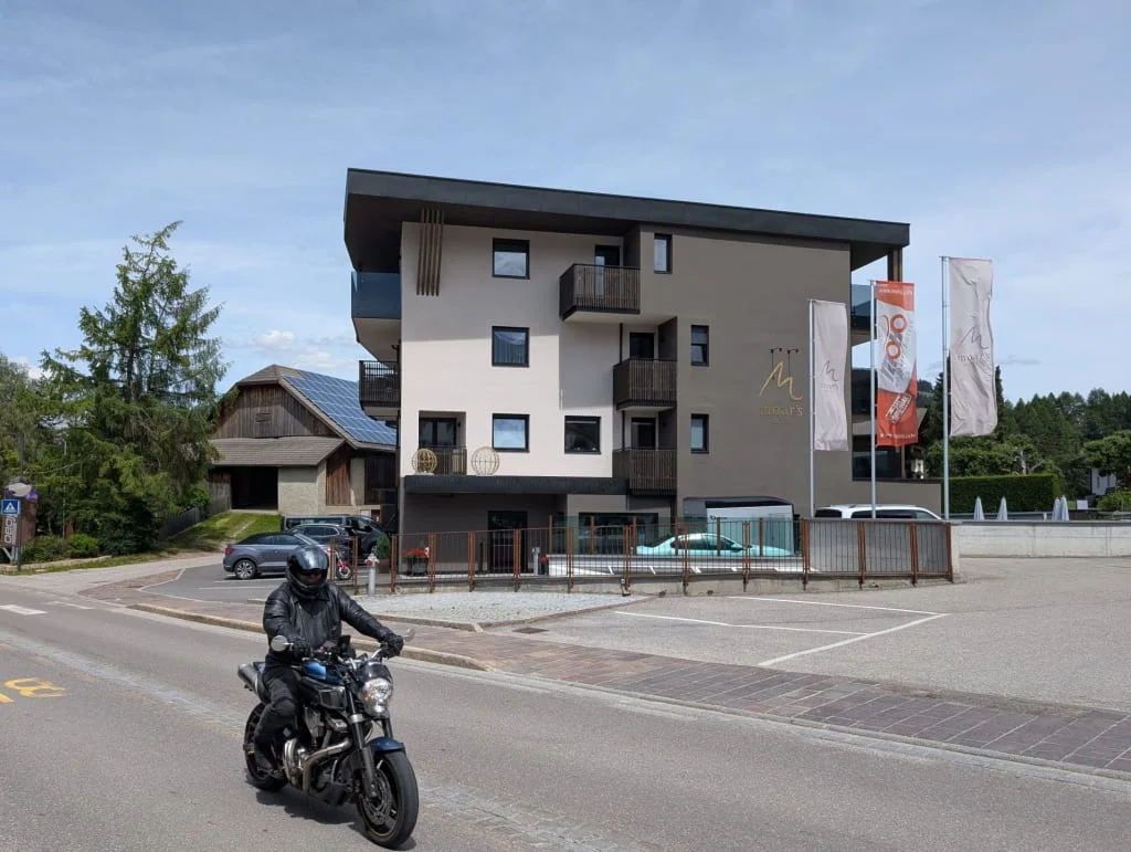 Moar's Bike & Relax Week Modern hotel building with balconies and flags by road with motorcyclist