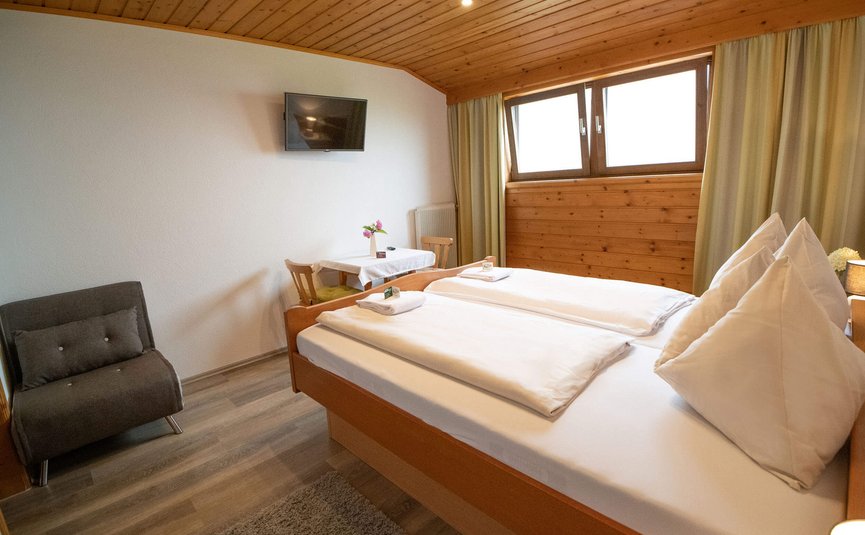 Gemütliches Schlafzimmer mit Doppelbett, Fernseher und kleiner Sitzgelegenheit