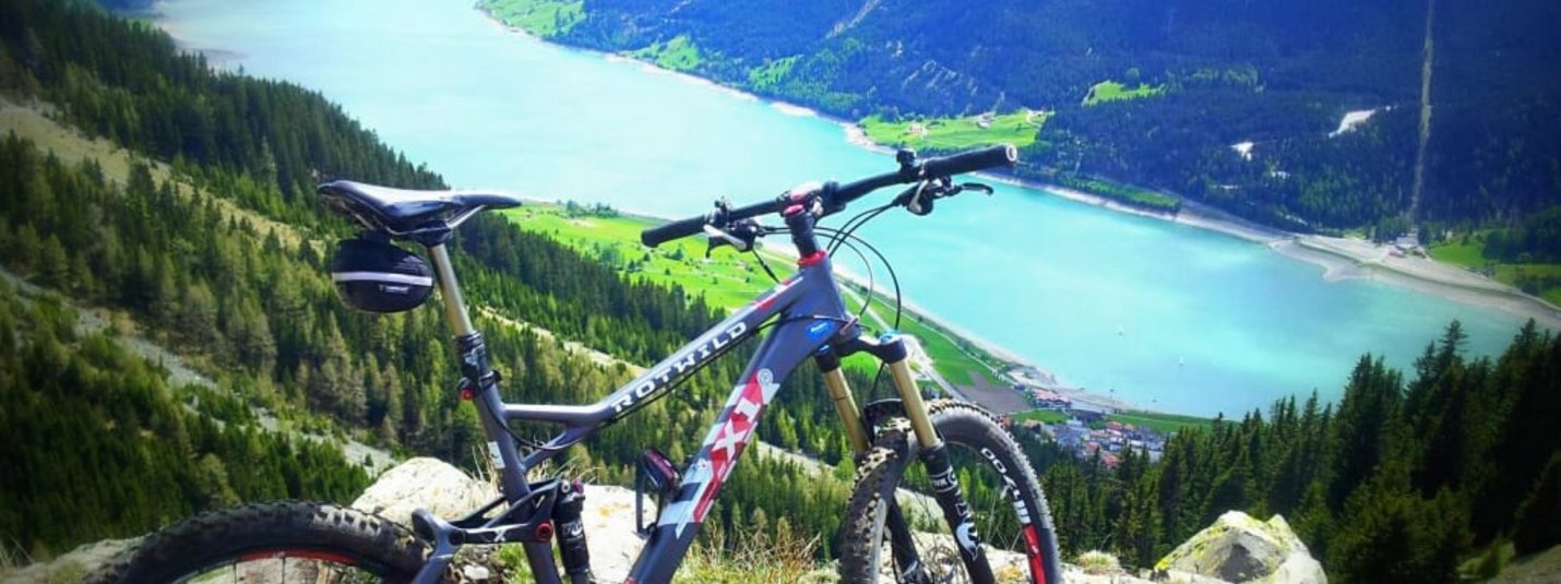 Trail Days Mountainbike auf Bergpfad mit Blick auf See und schneebedeckte Berge