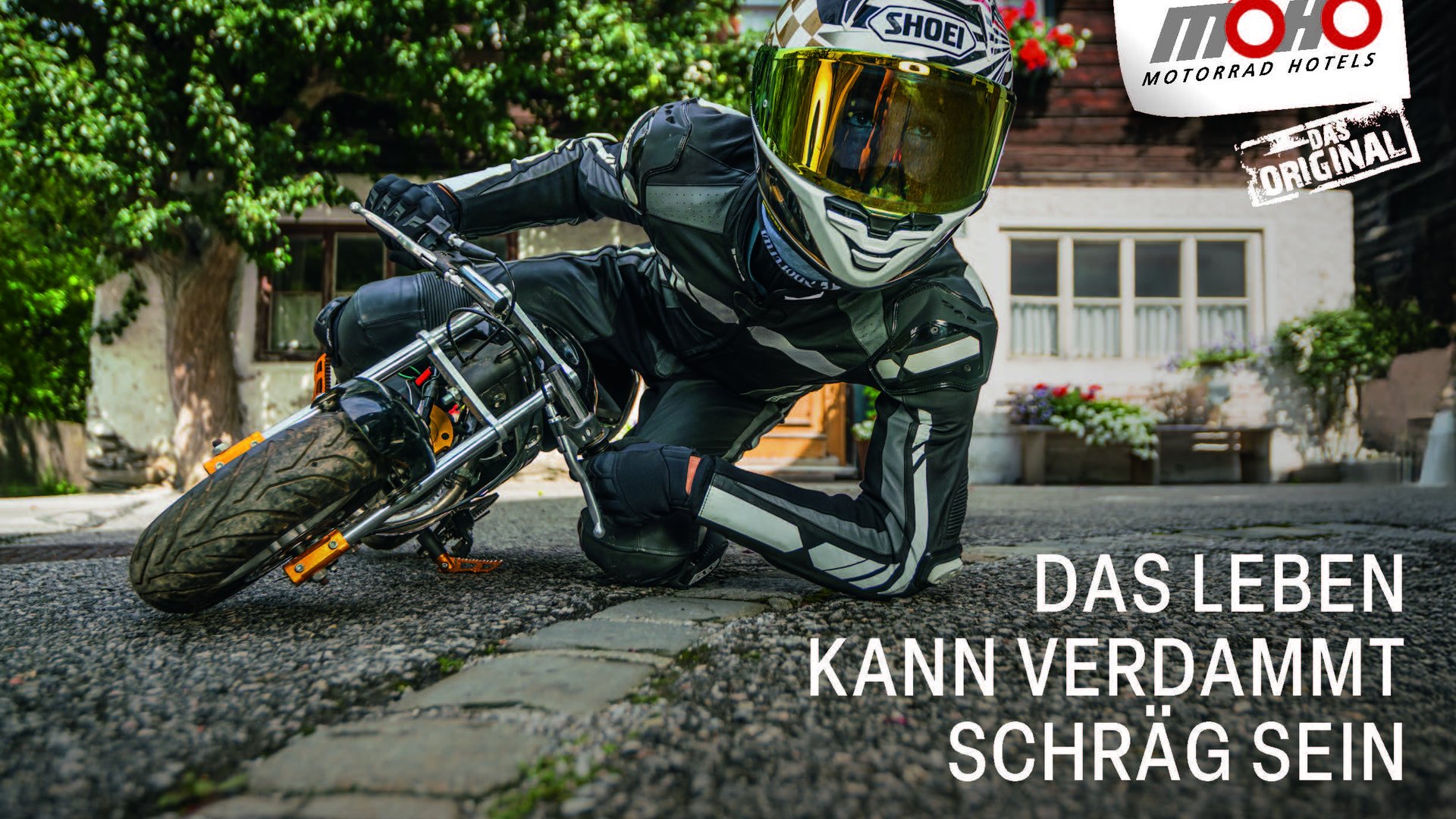 Motorradfahrer in voller Schutzkleidung fährt nah an Bordsteinkante auf Kopfsteinpflaster