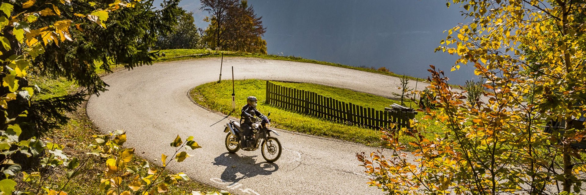 Motorradfahrer fährt durch eine kurvige Straße im herbstlichen Bergwald